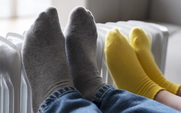 Deux paires de pieds portant des chaussettes, posées sur le radiateur.